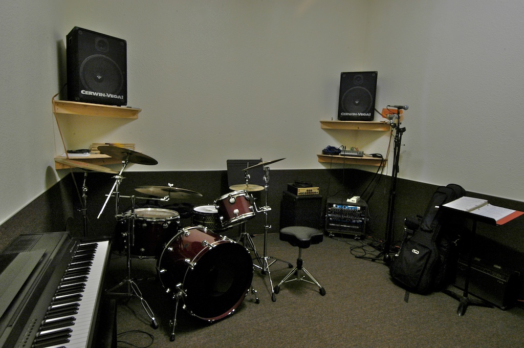 A music room set up with drums, keyboards, and speakers